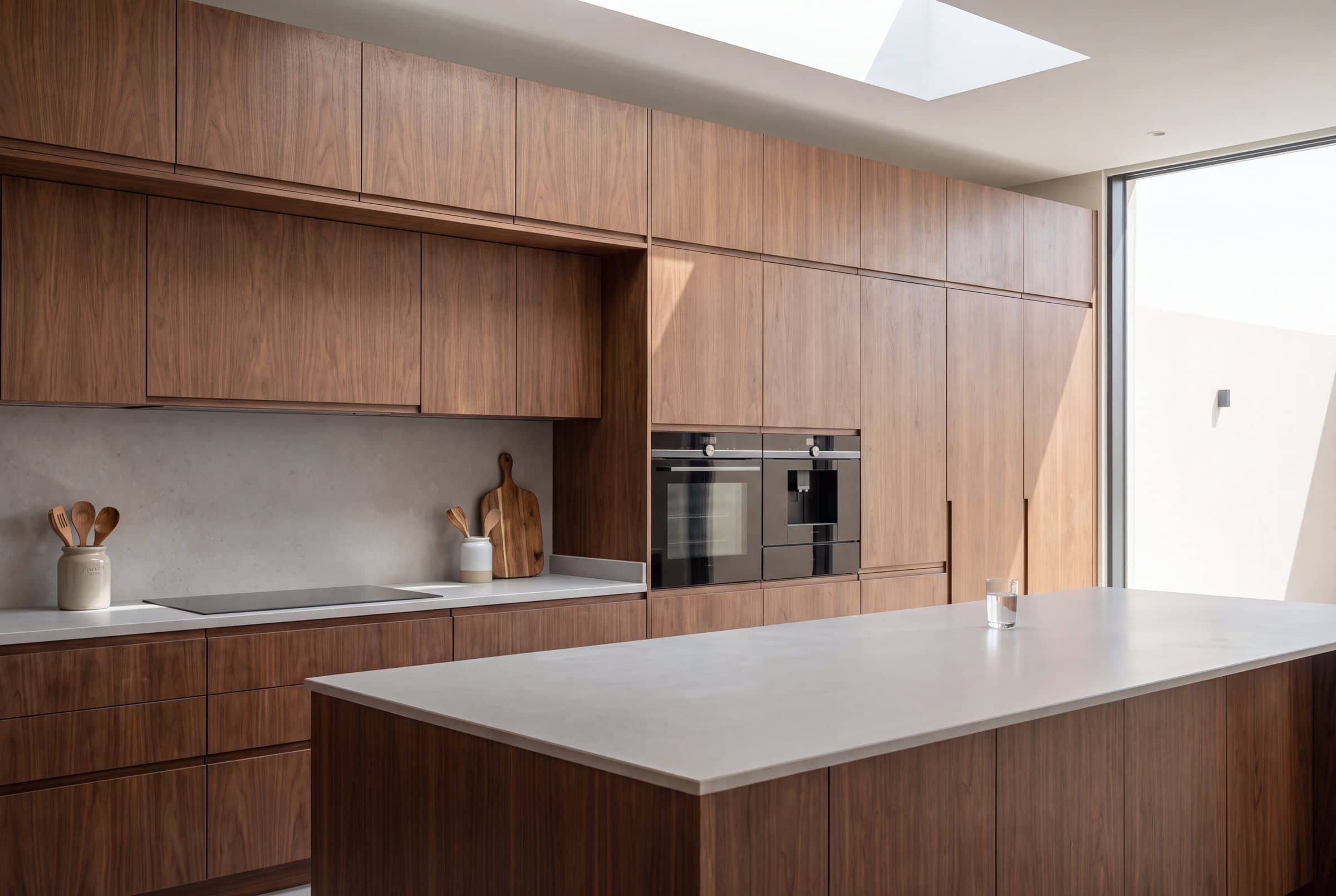 Walnut veneer kitchen with handleless doors, built-in ovens and a long island with a pale stone top